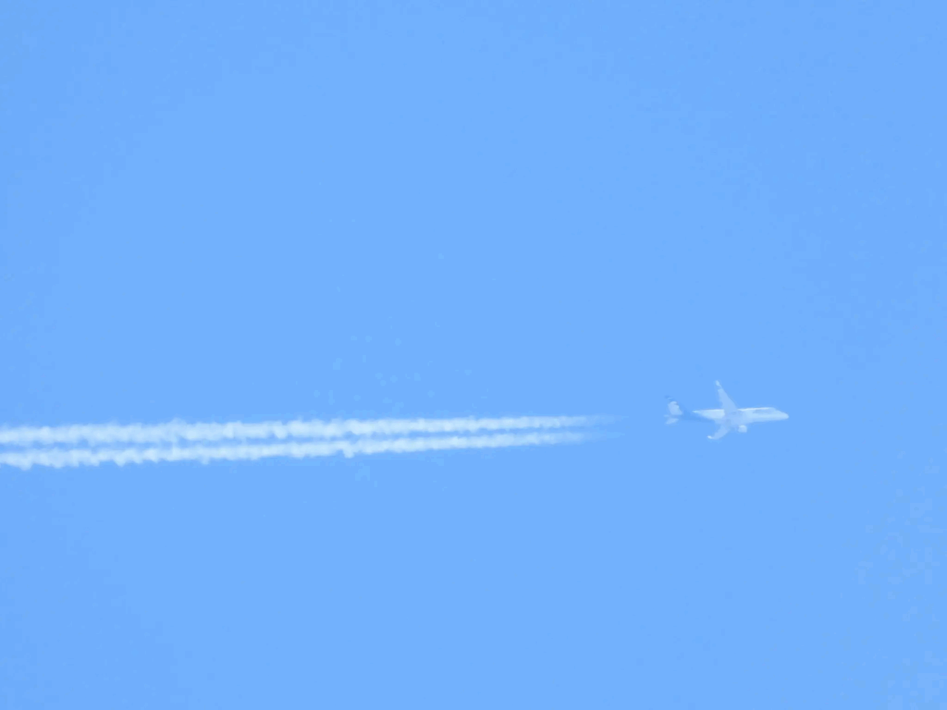 Airplane flying high, leaving a white vapor trail against a clear blue sky.