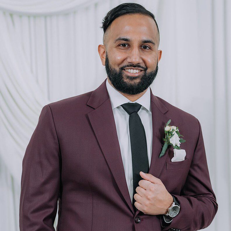 Man in maroon suit with boutonniere smiling.